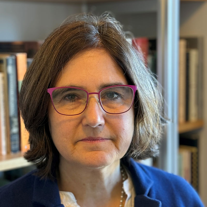 Anne Sartori sitting in front of a bookshelf wearing a blue blazer