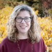 A smiling woman with glasses and curly blonde hair.